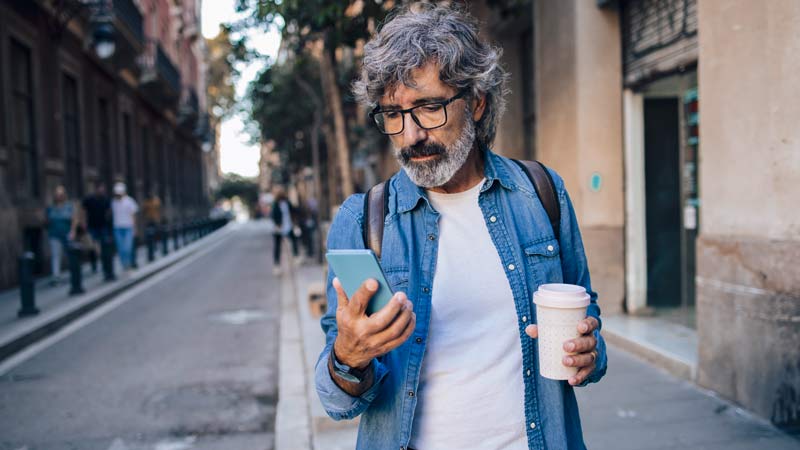 Plano médio de homem de meia idade a passear na rua e a olhar para o telefone com ar descontraído